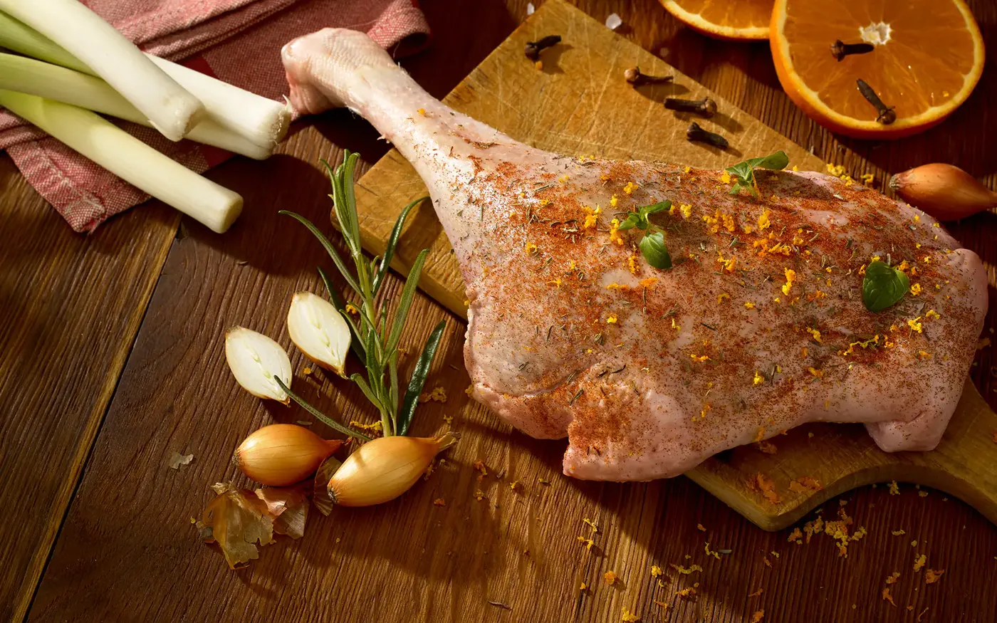 Gewürzte Gänsekeule mit Rosmarin, Schalotten und Orange auf einem Holzbrett